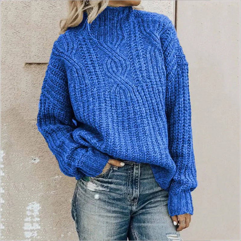 Femme portant un pull bleu en tricot torsadé, manches longues, col montant, associé à un jean décontracté. Mode automne-hiver tendance.