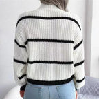 Femme portant un pull en tricot blanc à rayures noires, manches longues, avec un jean bleu. Mode automne-hiver, style décontracté et tendance.