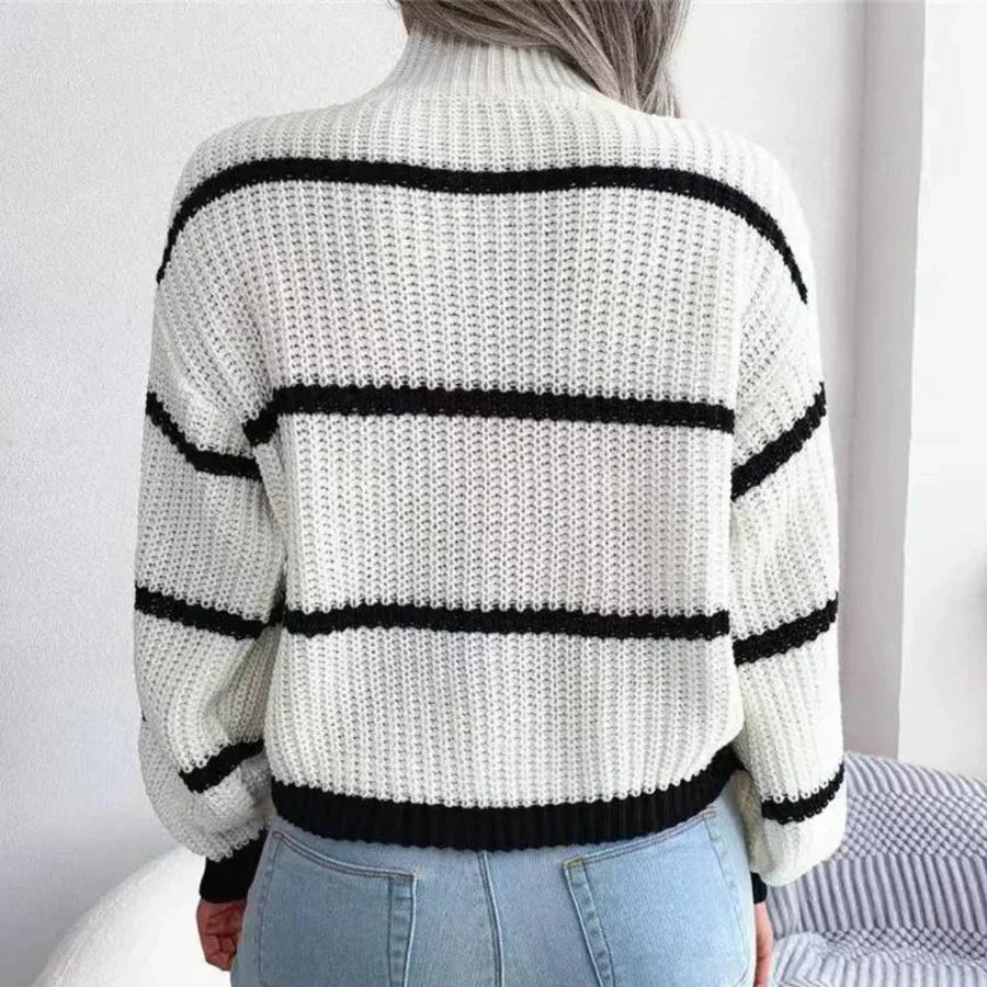 Femme portant un pull en tricot blanc à rayures noires, manches longues, avec un jean bleu. Mode automne-hiver, style décontracté et tendance.