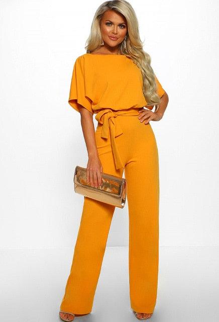 Femme en combinaison orange élégante, tenant une pochette dorée. Mode féminine chic, tenue tendance, style moderne.