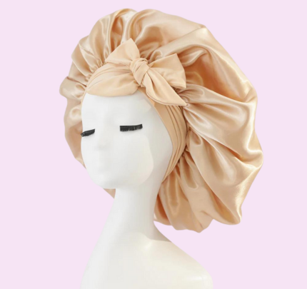 Mannequin portant un bonnet en satin doré avec un nœud, sur fond rose. Accessoire de mode élégant pour protéger les cheveux.