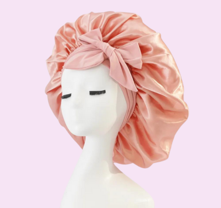 Mannequin portant un bonnet de satin rose avec un nœud, sur fond rose. Accessoire de mode élégant pour cheveux, protection nocturne.