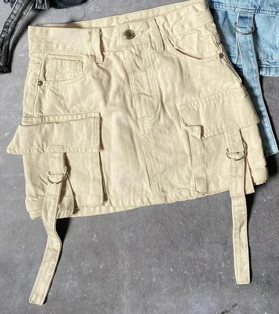Jupe cargo beige en denim avec poches à rabat et sangles, posée sur un fond gris. Mode tendance, style utilitaire, vêtements pour femmes.