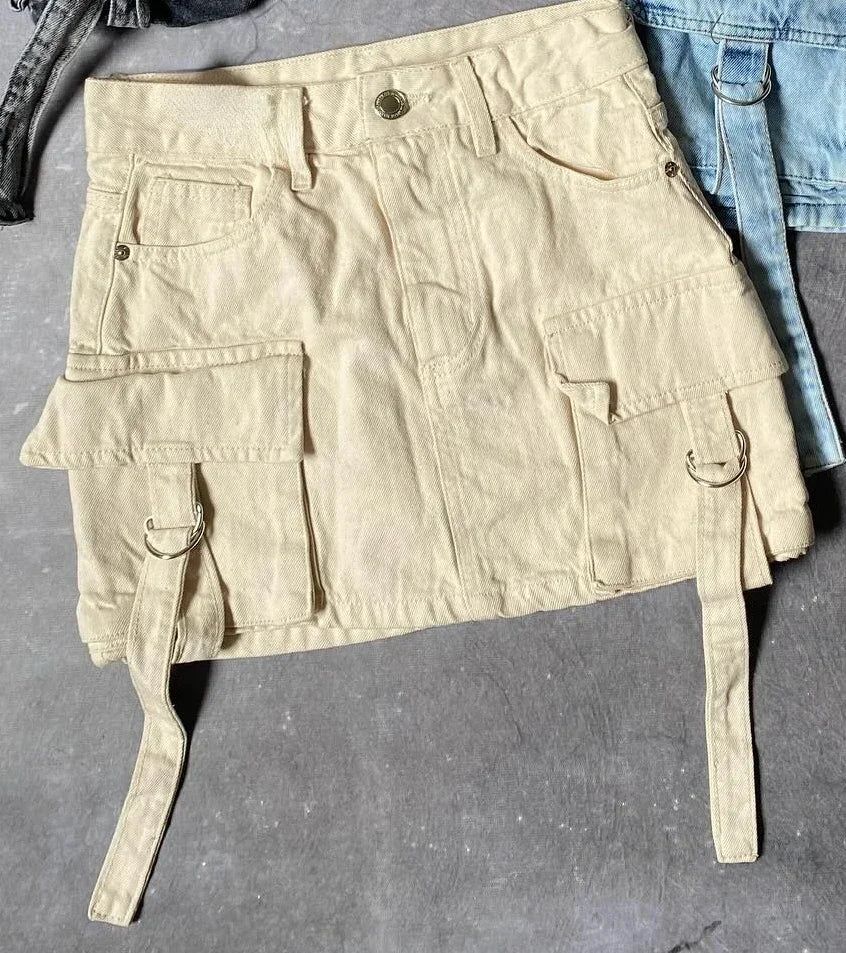 Jupe cargo beige en denim avec poches multiples et sangles, posée sur un fond gris. Mode urbaine, tendance utilitaire, style décontracté.