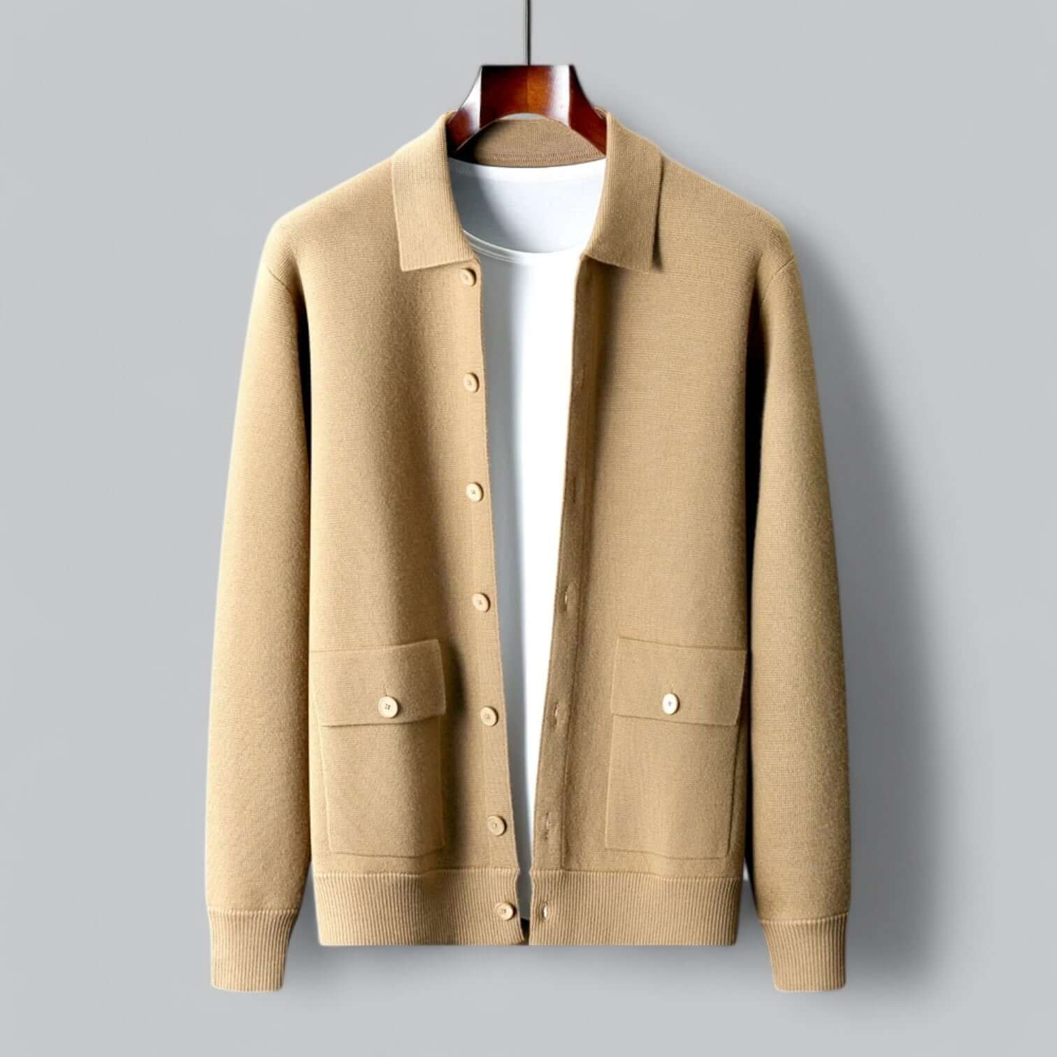 Cardigan beige en laine suspendu sur cintre, avec col classique et poches avant, sur fond gris. Mode automne-hiver, vêtement élégant et confortable.