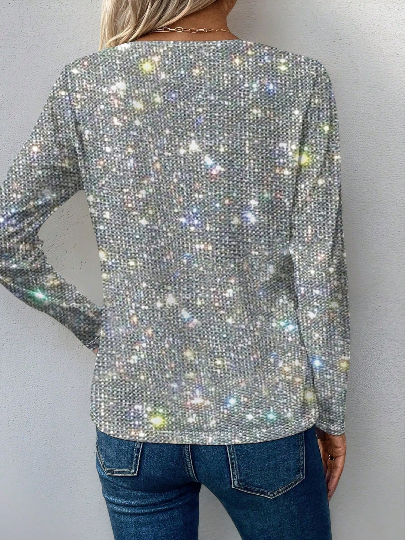 Femme portant un pull scintillant à manches longues, motif paillettes multicolores, dos tourné, avec un jean bleu. Mode tendance, style glamour.