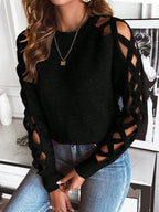 Femme portant un pull noir à manches ajourées et un jean bleu, posant dans un intérieur moderne. Mode automne, style chic et décontracté.