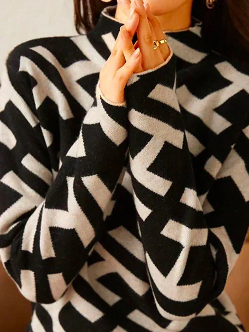 Femme portant un pull à col roulé noir et blanc avec motif géométrique en zigzag, manches longues, style moderne et élégant.