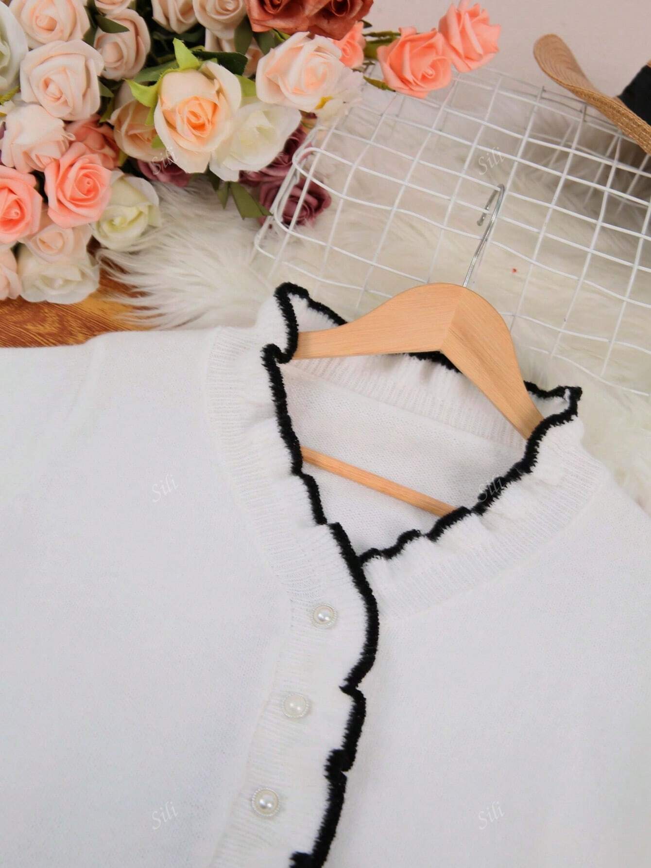 Gilet blanc à col volanté noir sur cintre, posé sur fond de fourrure blanche avec bouquet de roses multicolores. Mode féminine élégante et chic.