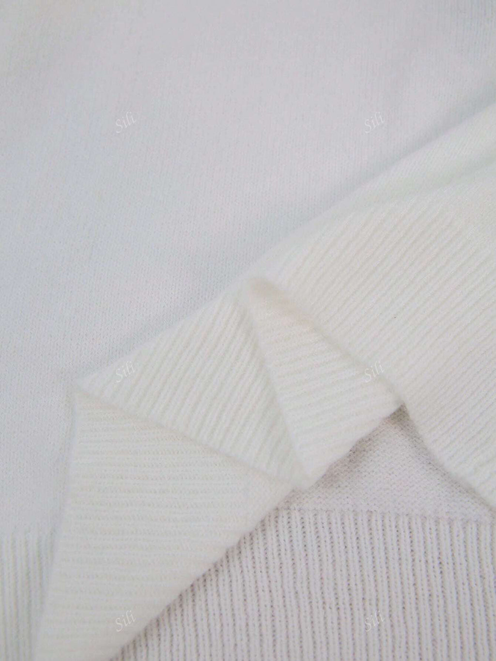 Pull en laine blanc texturé, gros plan sur les détails des mailles et des bords côtelés, style élégant et minimaliste.