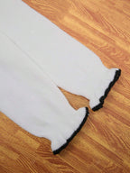 Pantalon blanc en tricot pour bébé avec bordures noires, posé sur un sol en bois. Vêtements pour enfants, mode bébé, pantalon confortable.