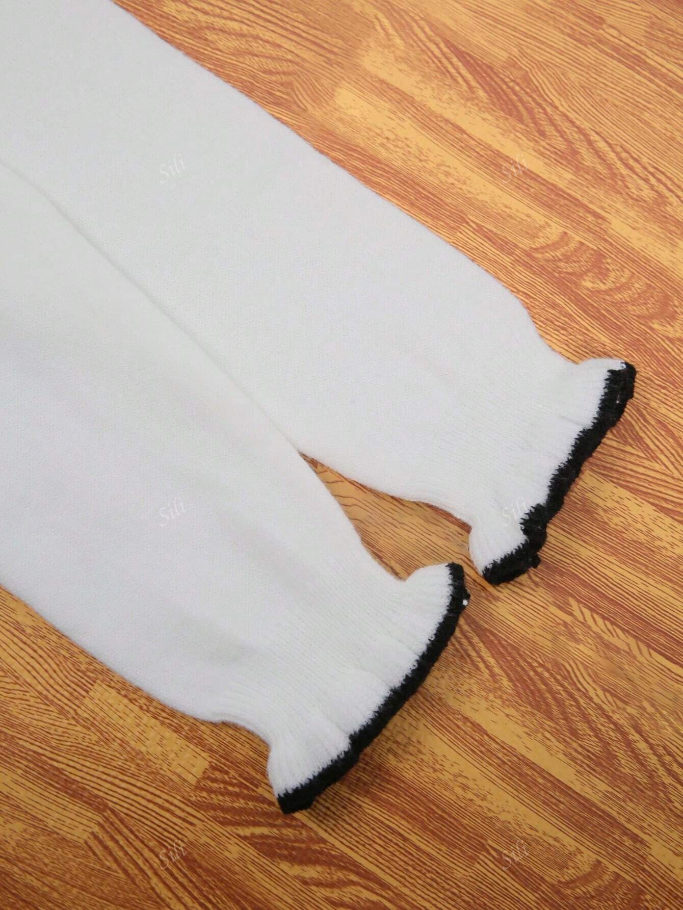 Pantalon blanc en tricot pour bébé avec bordures noires, posé sur un sol en bois. Vêtements pour enfants, mode bébé, pantalon confortable.