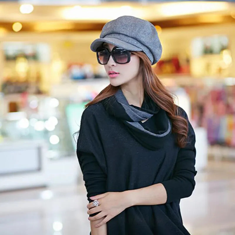 Femme élégante portant un béret gris, lunettes de soleil noires et écharpe, dans un centre commercial lumineux. Mode automne chic, accessoires tendance.
