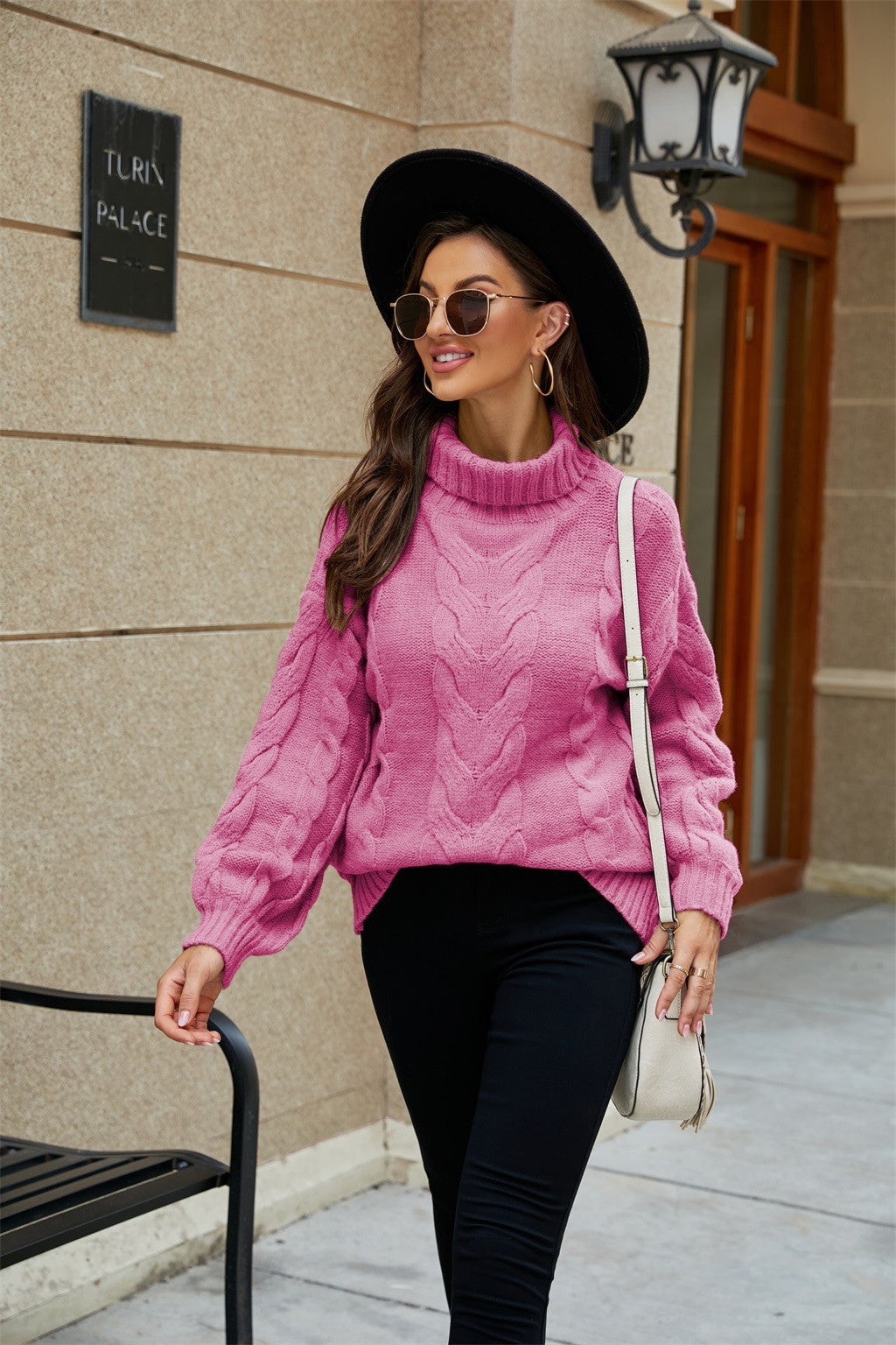 Femme élégante en pull rose à col roulé, chapeau noir et lunettes de soleil, marchant en ville. Mode automne, style urbain chic.