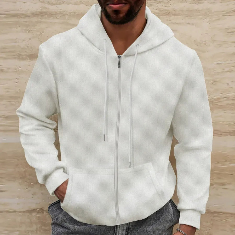 Homme portant un sweat à capuche blanc zippé, mains dans les poches, devant un mur beige. Mode décontractée, style urbain, vêtements pour hommes.