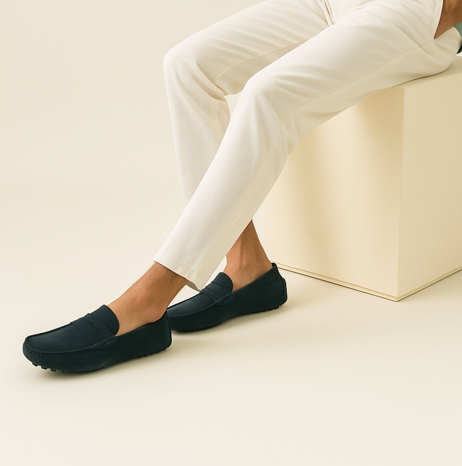Pantalon blanc élégant avec mocassins noirs en cuir, style moderne et minimaliste, mode masculine, assis sur un cube beige.