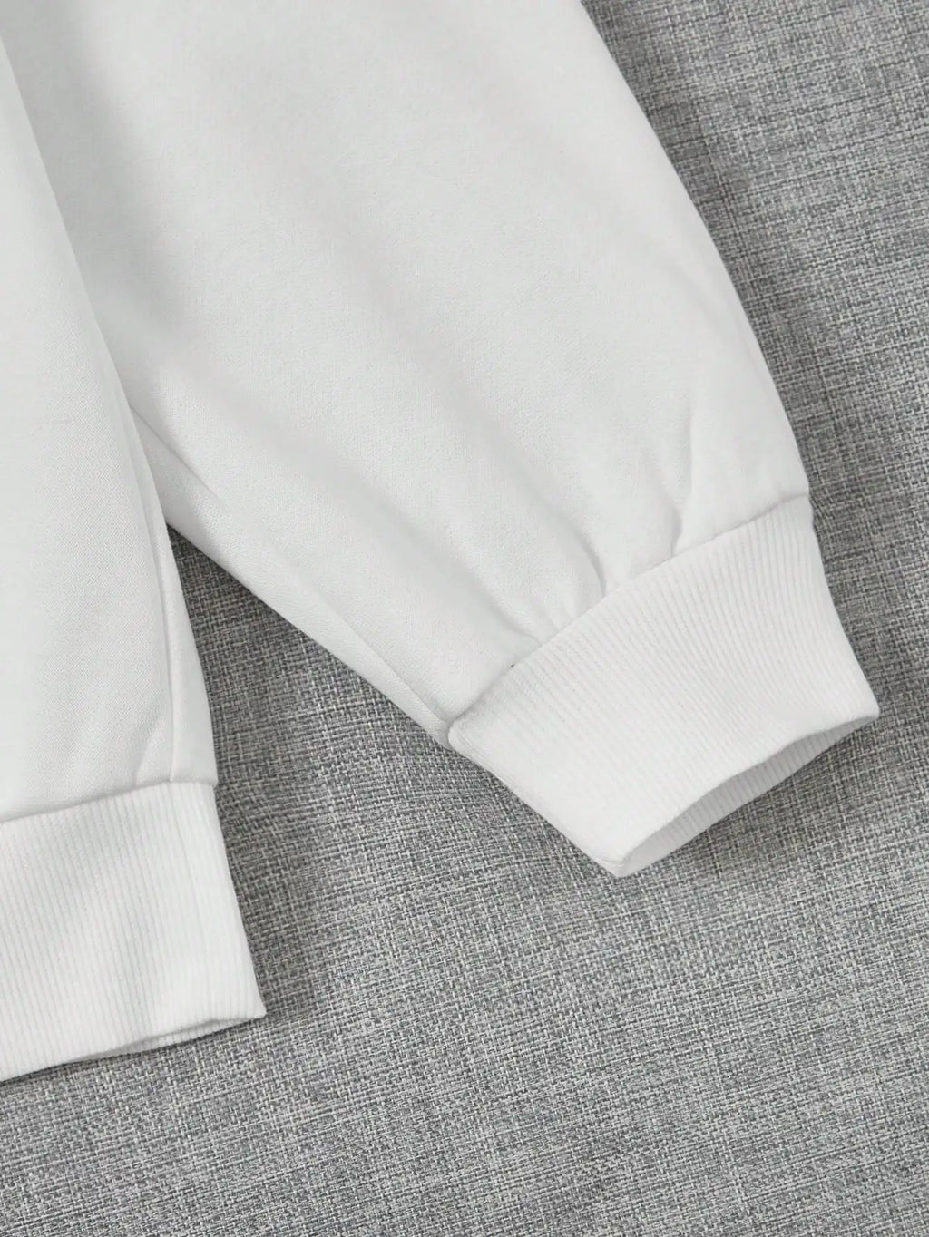 Manche de sweat-shirt blanc en coton sur fond gris, mode décontractée, vêtement confortable, style minimaliste, tendance automne-hiver.