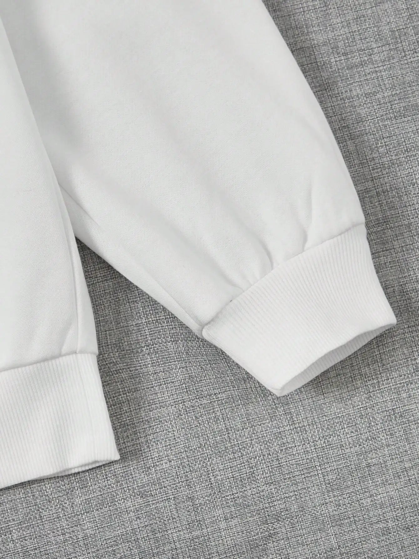 Manche de sweat-shirt blanc en coton sur fond gris, mode décontractée, vêtement confortable, style minimaliste, tendance automne-hiver.