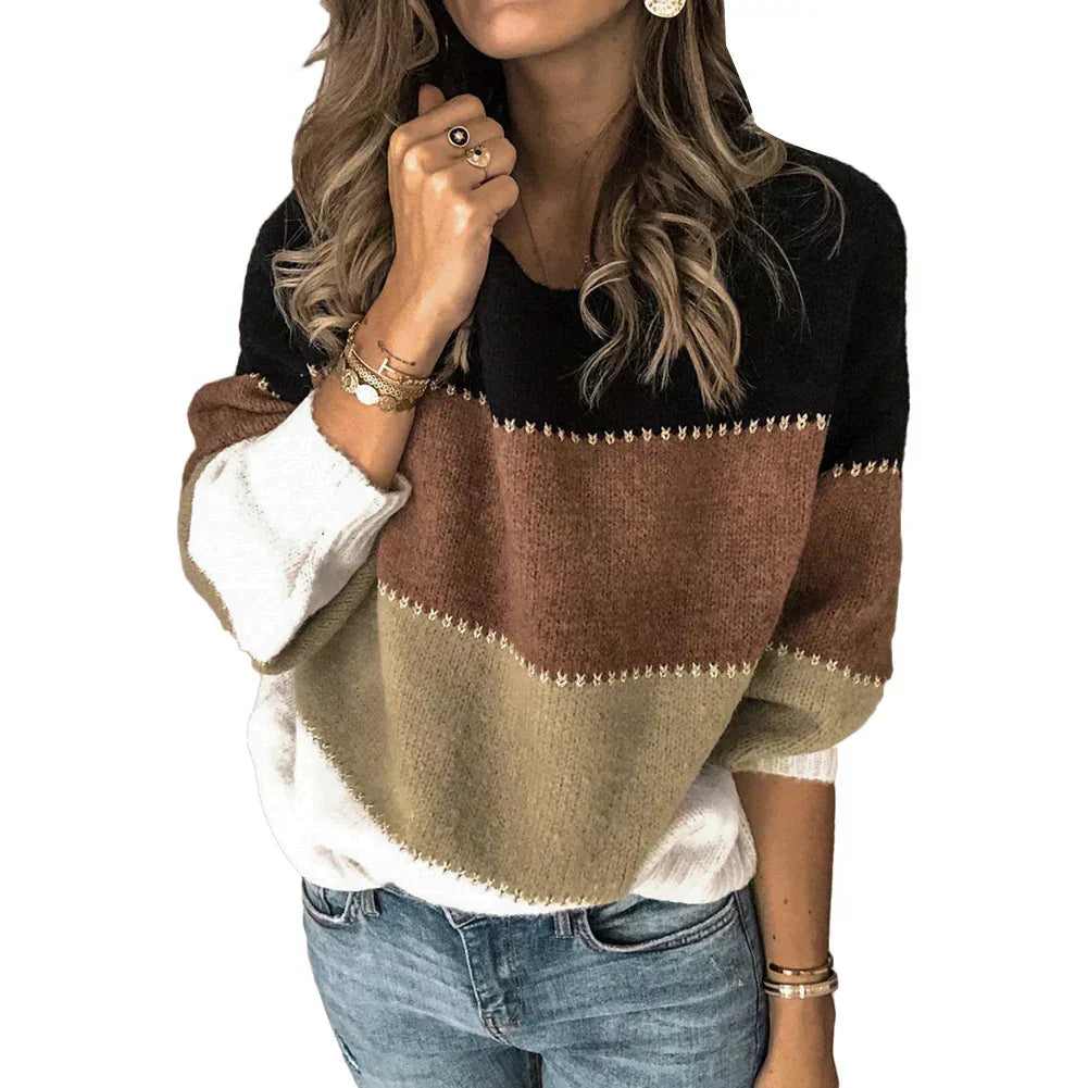 Femme portant un pull tricolore à rayures noires, marron et beige, manches longues, avec des bijoux dorés, posant en jean. Mode automne-hiver tendance.
