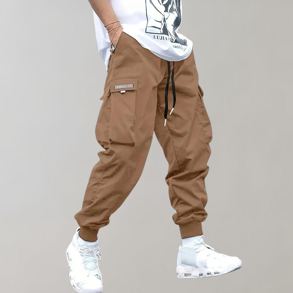 Pantalon cargo marron pour homme avec poches latérales, cordon de serrage noir, porté avec des baskets blanches et un t-shirt blanc.