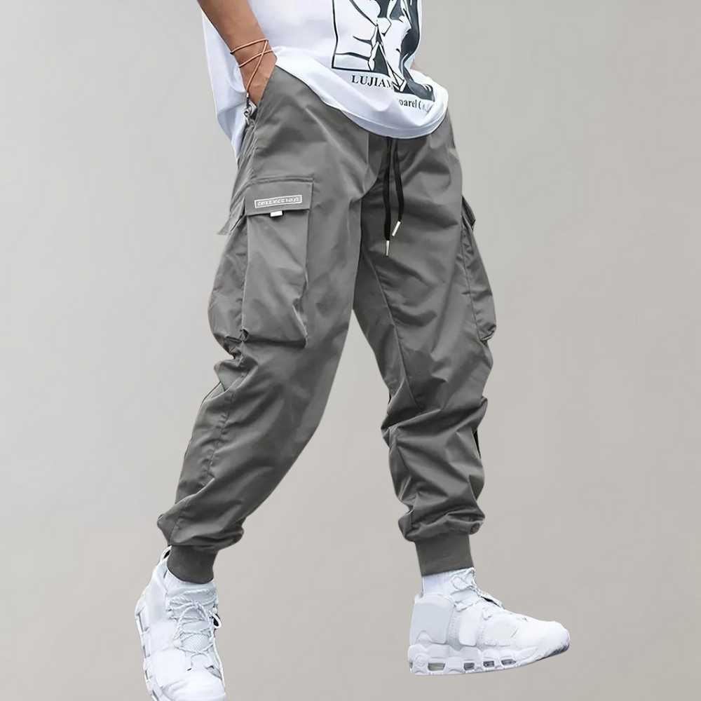 Pantalon cargo gris pour homme, style décontracté, avec poches latérales, cordon de serrage, porté avec des baskets blanches modernes.