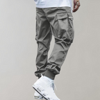 Pantalon cargo gris pour homme avec poches latérales, style décontracté, associé à des baskets blanches modernes. Mode urbaine tendance.