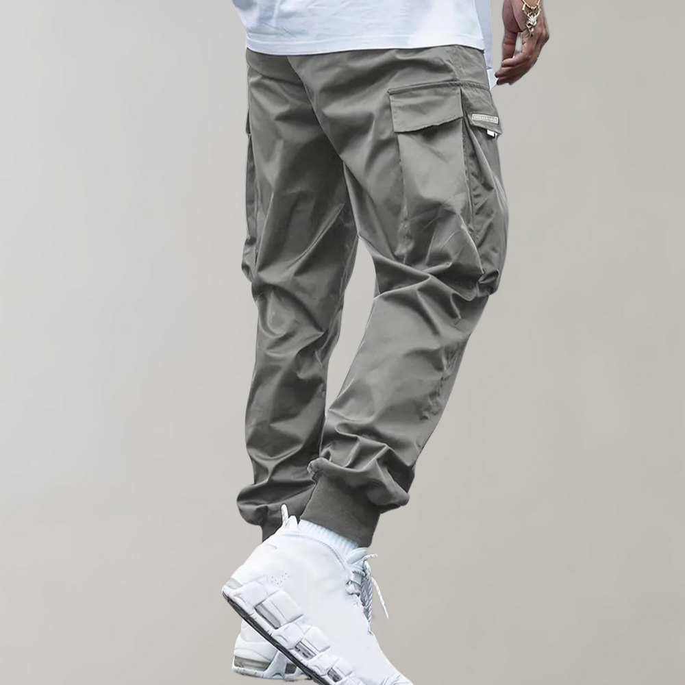 Pantalon cargo gris pour homme avec poches latérales, style décontracté, associé à des baskets blanches modernes. Mode urbaine tendance.