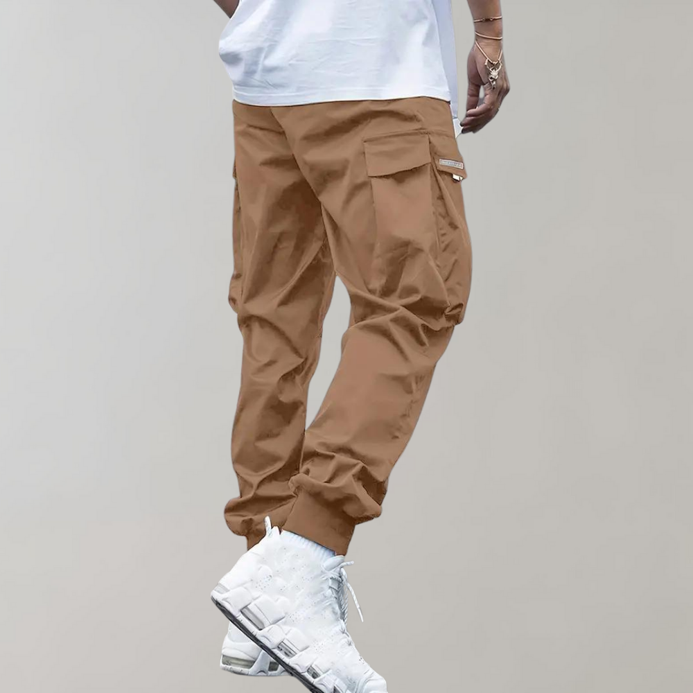 Pantalon cargo marron pour homme, coupe décontractée, poches latérales, porté avec des baskets blanches modernes, style urbain tendance.