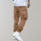 Pantalon cargo marron pour homme, coupe décontractée, poches latérales, porté avec des baskets blanches modernes, style urbain tendance.