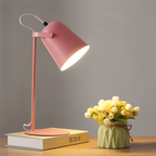 Lampe de bureau rose moderne éclairant un livre, à côté d'un vase vert avec des tulipes blanches, sur une table en bois. Décoration intérieure élégante.