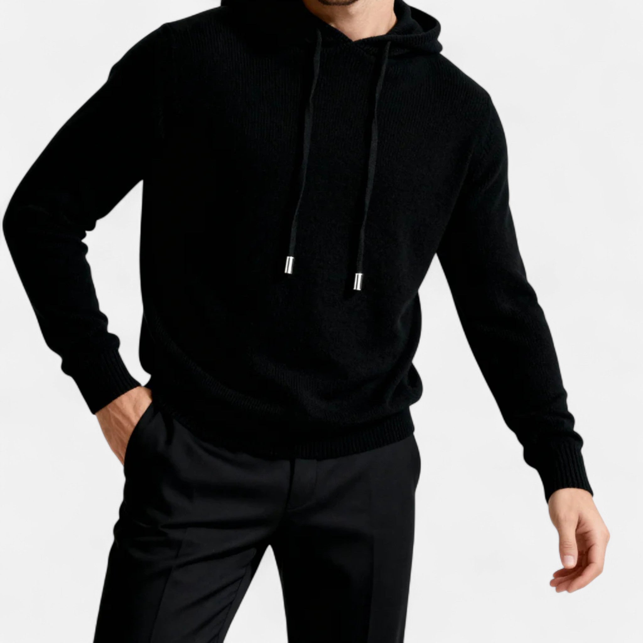 Homme portant un pull à capuche noir élégant, manches longues, avec cordons, associé à un pantalon noir. Mode masculine moderne et chic.