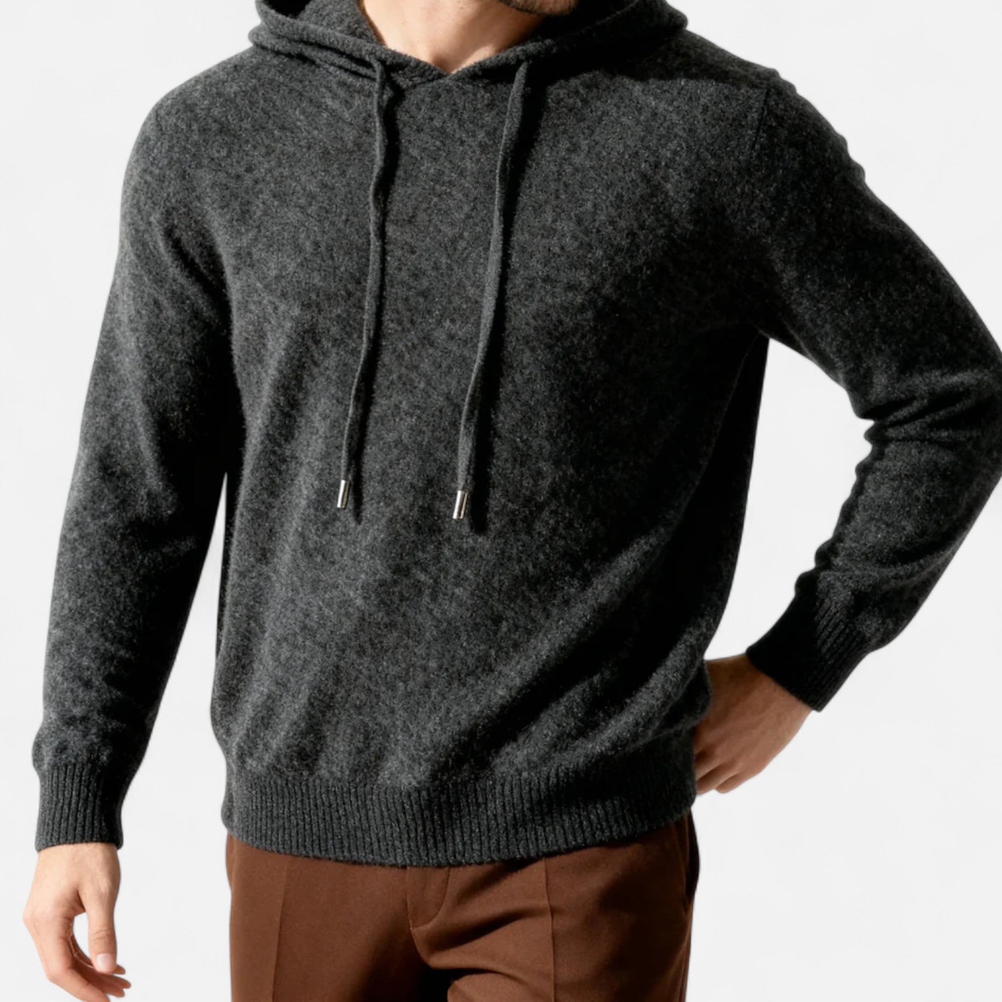 Homme portant un pull à capuche en laine gris foncé, manches longues, avec cordons, sur fond blanc. Mode masculine, vêtement hiver élégant.