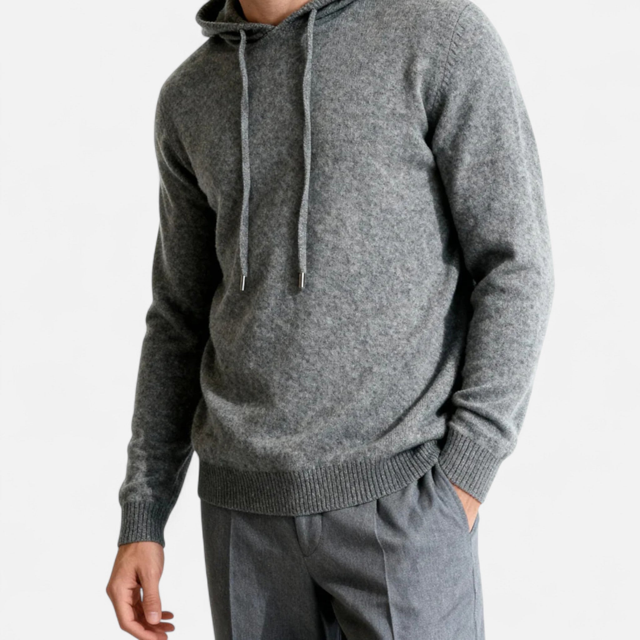 Homme portant un pull à capuche gris en laine, manches longues, avec cordons, assorti à un pantalon gris. Mode masculine élégante et décontractée.