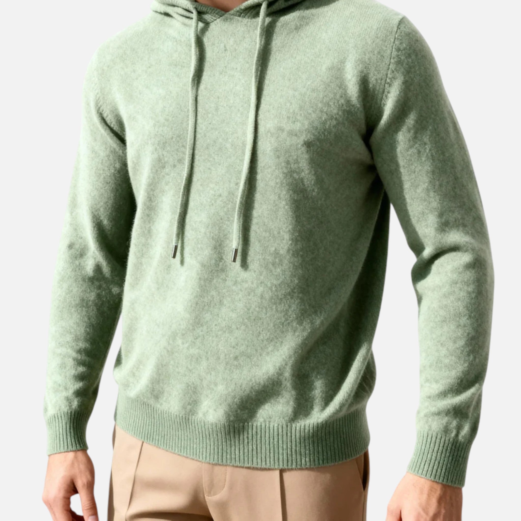 Homme portant un pull à capuche vert en laine, manches longues, avec cordons, assorti à un pantalon beige. Mode masculine élégante et décontractée.