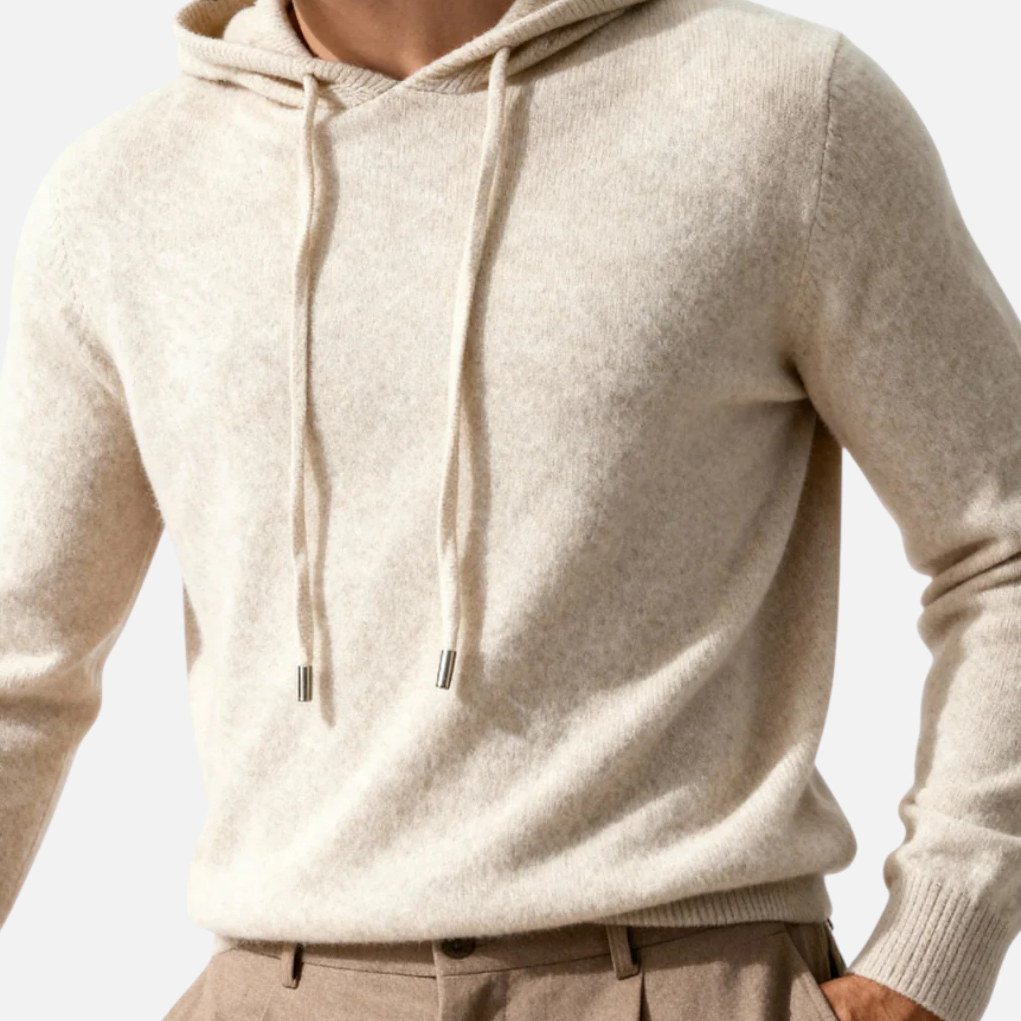 Homme portant un pull à capuche en cachemire beige, manches longues, avec cordons, sur fond neutre. Mode masculine élégante et confortable.