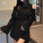 Femme en pull noir à épaules dénudées et manches évasées, jupe noire asymétrique, posant devant une porte. Mode élégante et moderne.