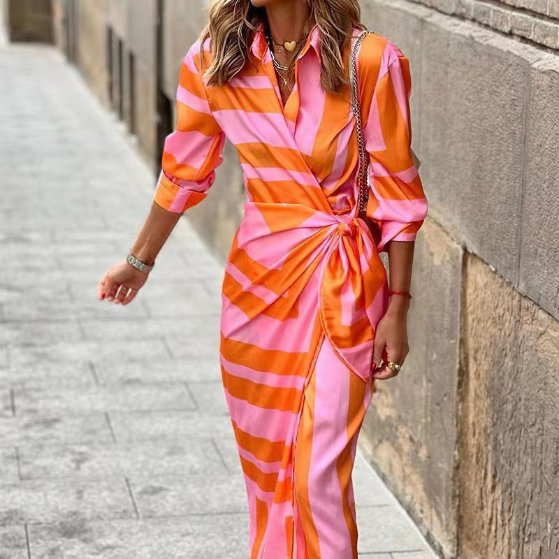 Robe longue à rayures roses et oranges, manches longues, ceinture nouée, femme marchant dans une rue pavée. Mode élégante et colorée.
