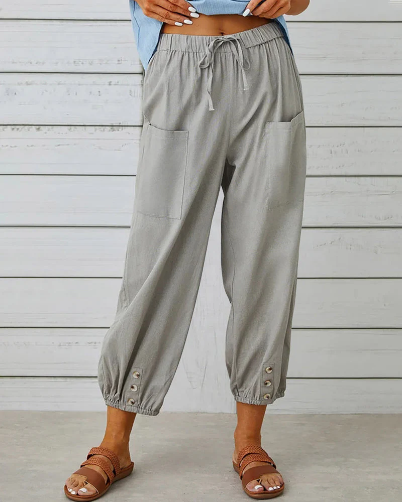 Pantalon ample gris avec poches avant, boutons décoratifs aux chevilles, porté avec des sandales marron. Mode décontractée femme, tendance été.