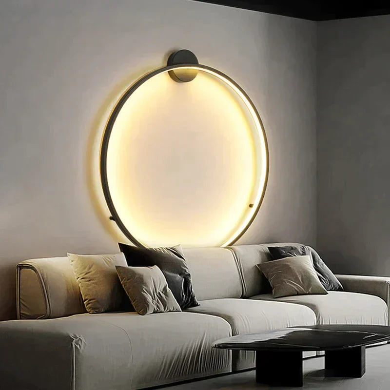 Lampe murale circulaire LED moderne éclairant un salon élégant avec canapé gris et coussins, créant une ambiance chaleureuse et contemporaine.
