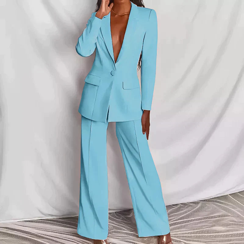 Femme portant un costume bleu clair élégant, veste à un bouton, pantalon large, posant sur fond blanc. Mode féminine, tenue chic, style moderne.