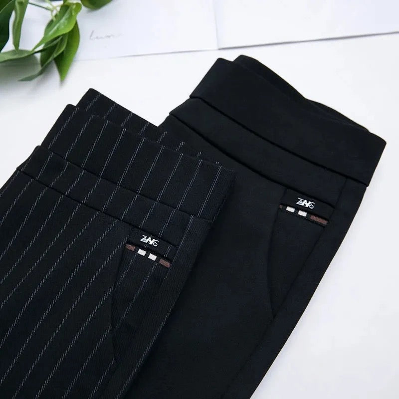 Deux pantalons élégants pour femmes, l'un noir uni et l'autre à rayures, posés sur une surface blanche avec une plante verte en arrière-plan.