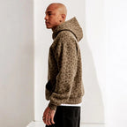 Homme portant un sweat à capuche imprimé léopard marron, style décontracté, mode urbaine, tendance automne-hiver, profil gauche, intérieur minimaliste.
