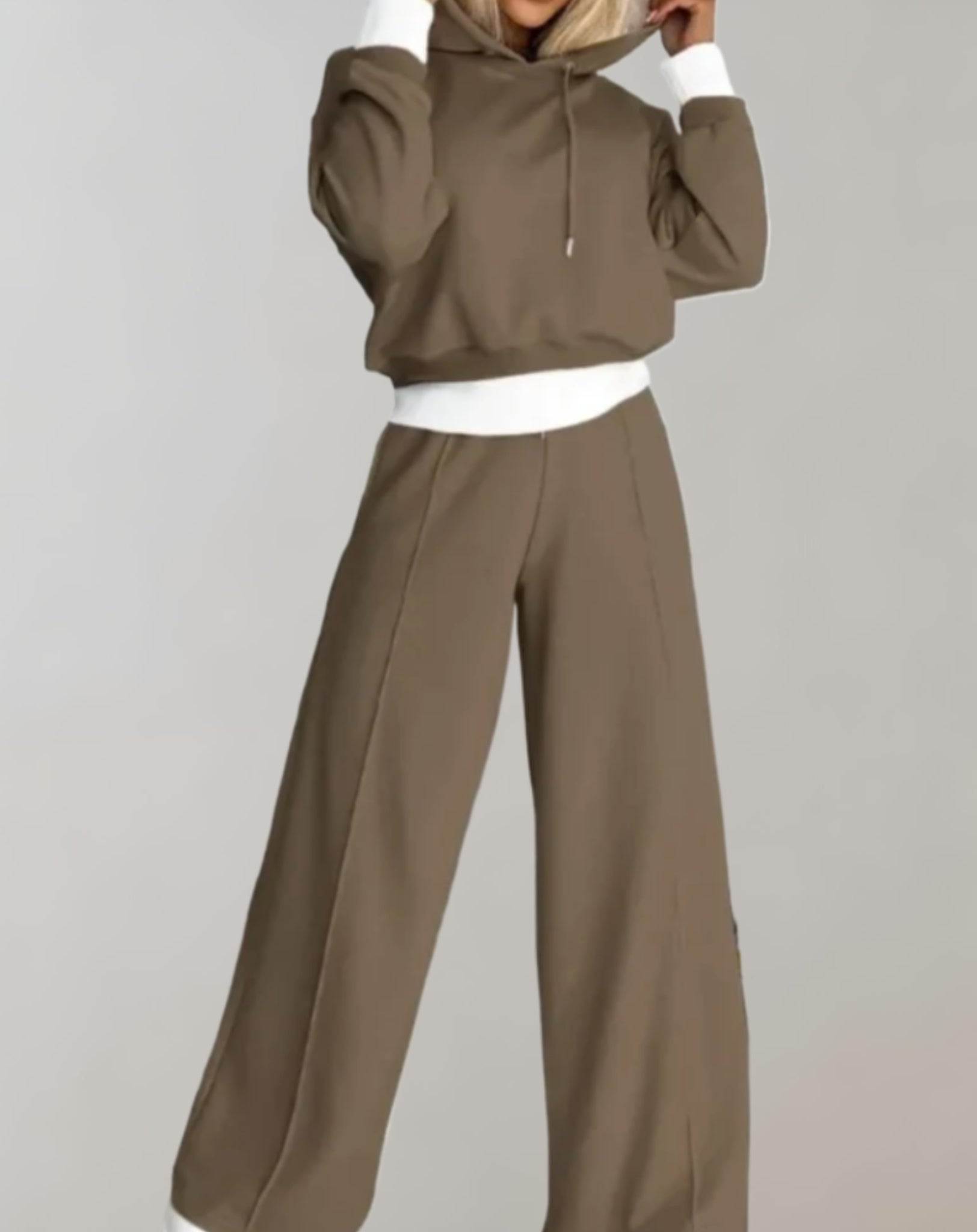 Femme portant un ensemble de survêtement marron avec capuche, taille élastique et ourlets blancs contrastants. Mode décontractée, tendance automne.