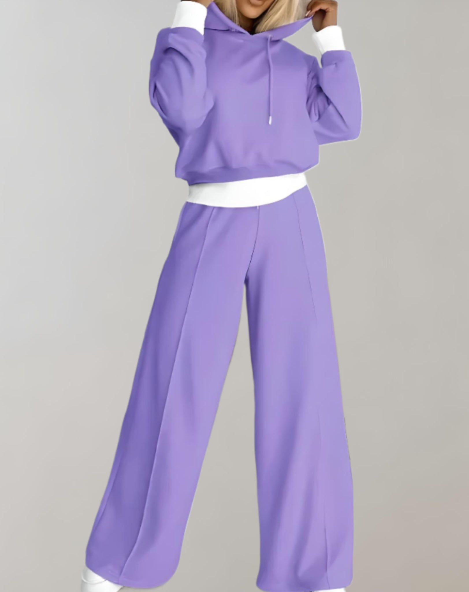 Femme portant un ensemble de survêtement violet, composé d'un sweat à capuche et d'un pantalon ample. Mode décontractée, tendance automne-hiver.