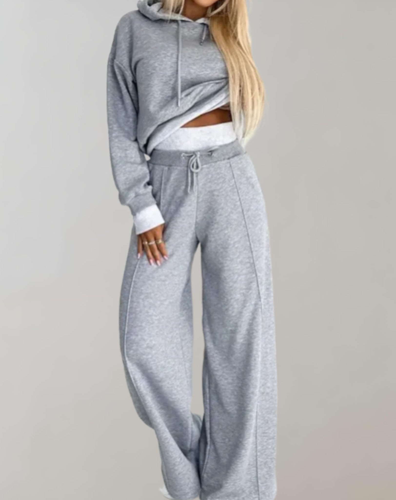Femme portant un ensemble de survêtement gris, composé d'un sweat à capuche et d'un pantalon ample. Mode décontractée, tendance streetwear.