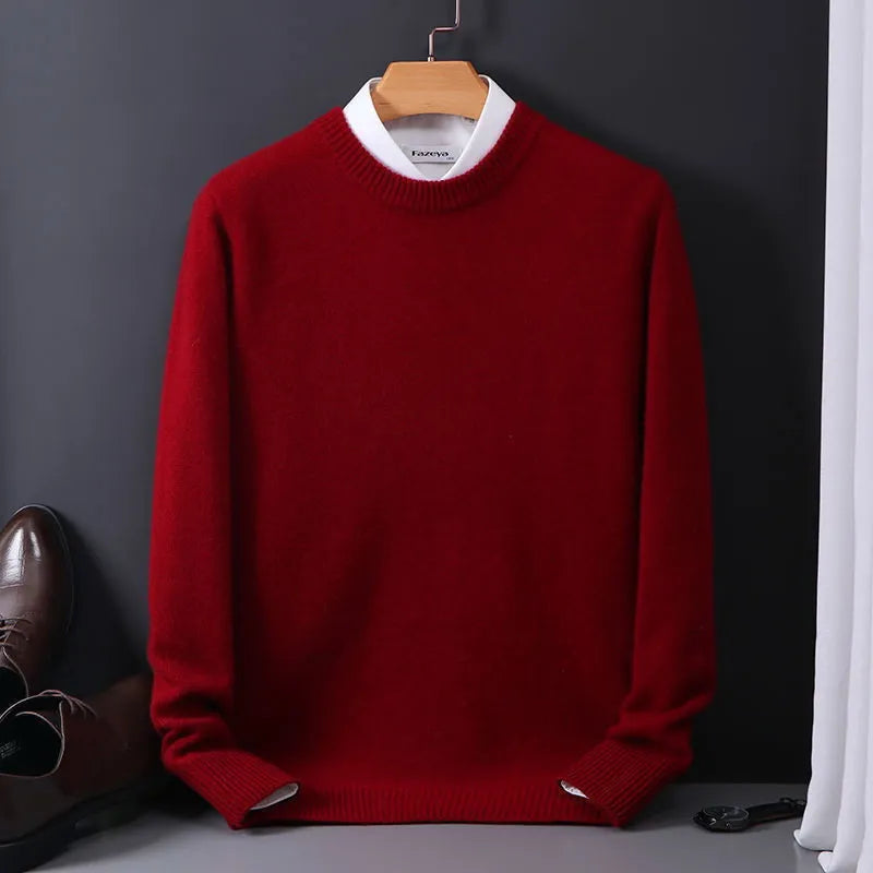 Pull-over rouge en laine sur cintre, chemise blanche visible au col, posé contre un mur sombre. Chaussures marron et rideau blanc en arrière-plan.