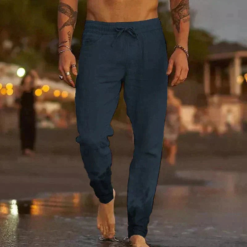 Homme marchant sur la plage au crépuscule, portant un pantalon de jogging bleu marine. Mode décontractée, soirée d'été, style masculin tendance.