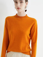Jeune femme portant un pull orange vif en laine, manches longues, col rond, posant contre un fond blanc. Mode automne, style élégant et moderne.