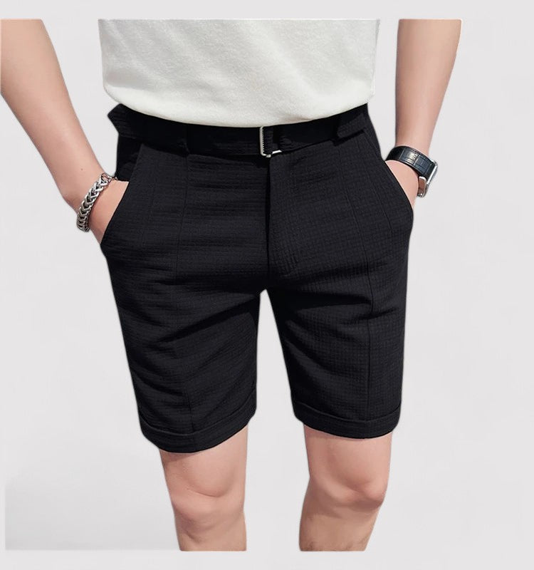 Homme portant un short noir élégant avec ceinture, mains dans les poches, bracelet argenté et montre noire, mode masculine moderne.