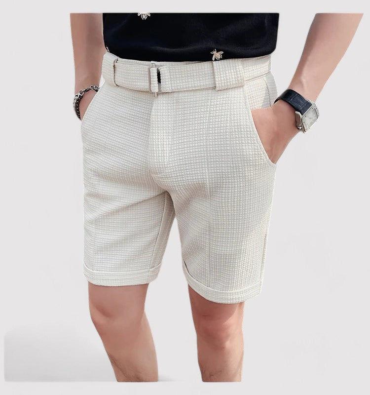 Short beige homme élégant, ceinture assortie, montre noire, style décontracté chic, mode estivale, tenue moderne, fond blanc.